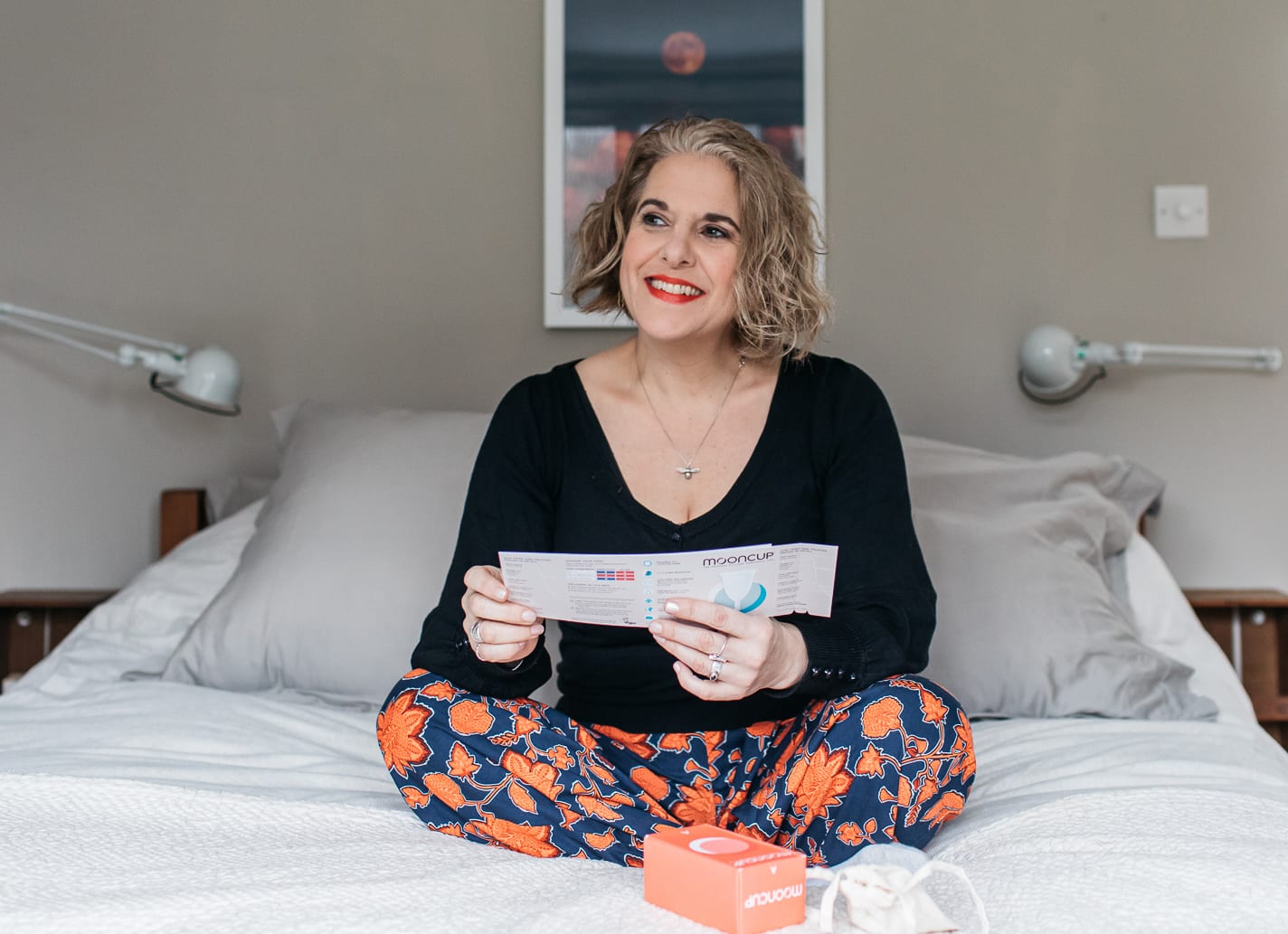 Perimenopausal woman sat on her bed holding Mooncup menstrual cup instructions.