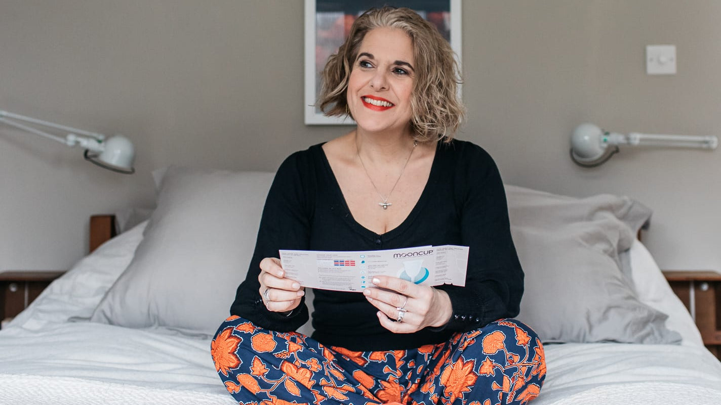 Perimenopausal woman sat on her bed holding Mooncup menstrual cup instructions.