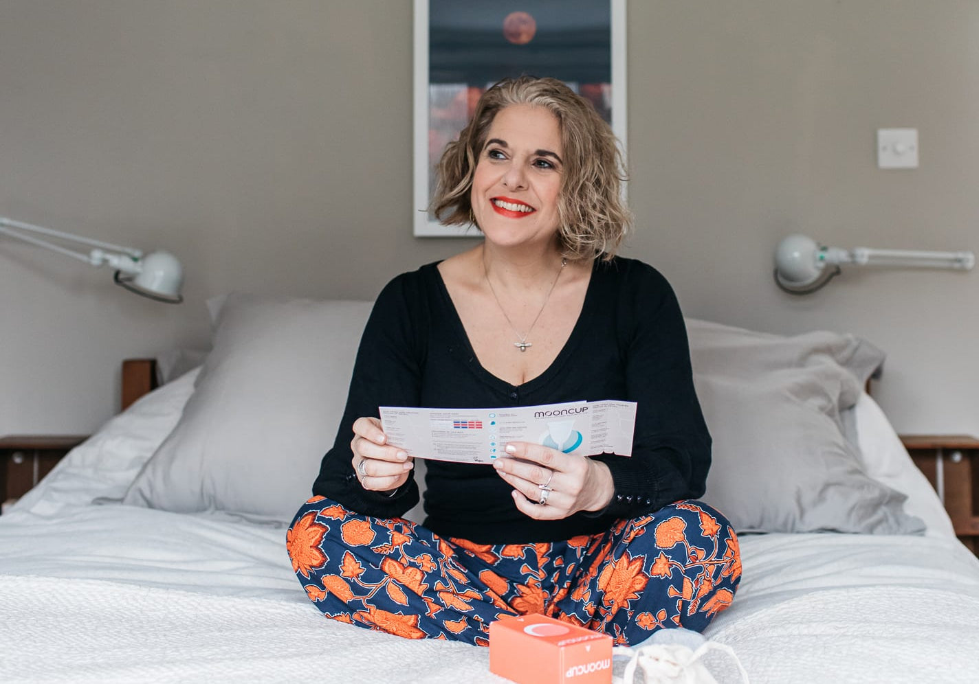 Perimenopausal woman sat on her bed holding Mooncup menstrual cup instructions.