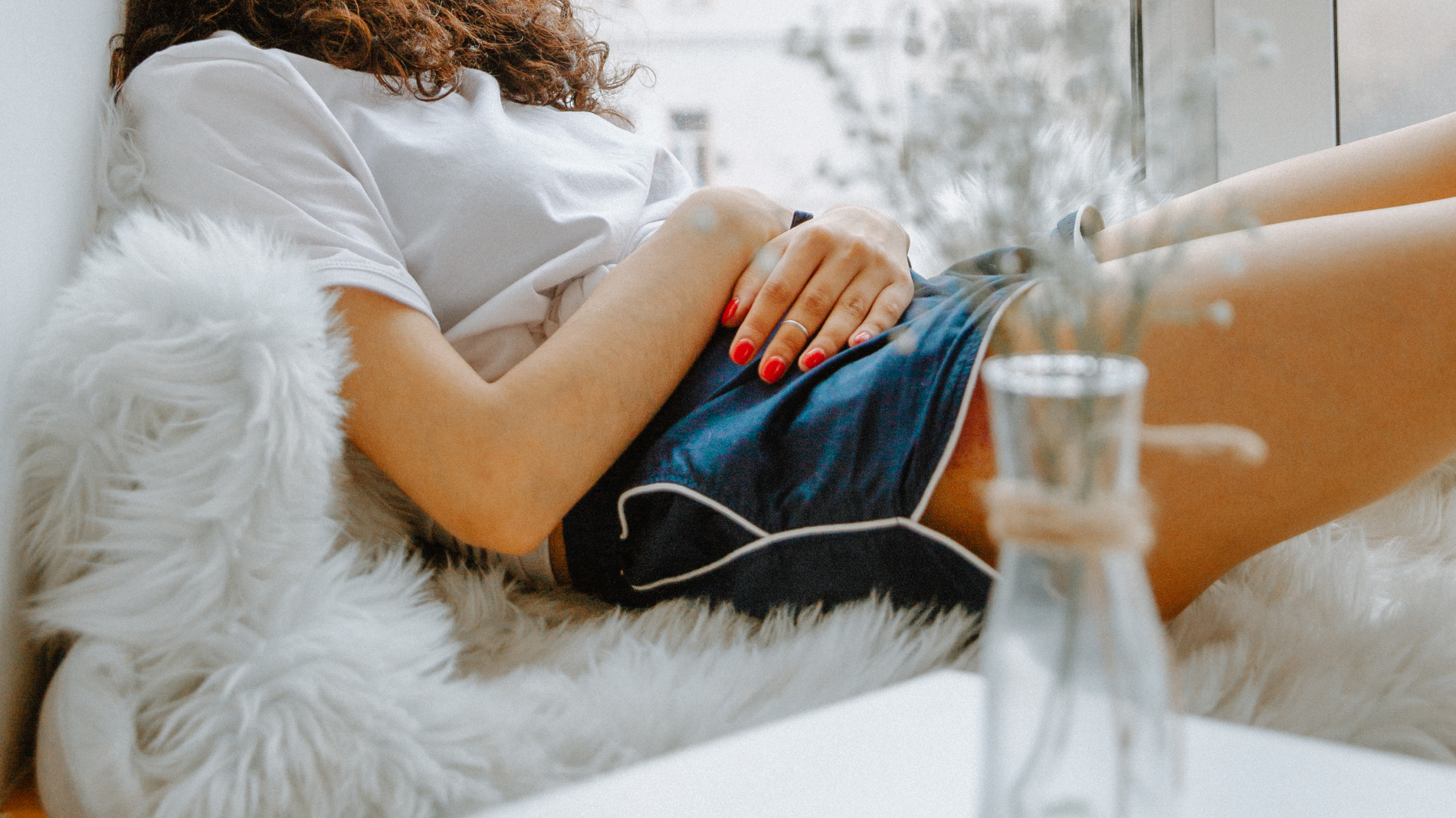 Woman lying down holding her stomach — supporting blog about period bloating, its causes, and how to reduce menstrual discomfort through lifestyle and dietary changes.