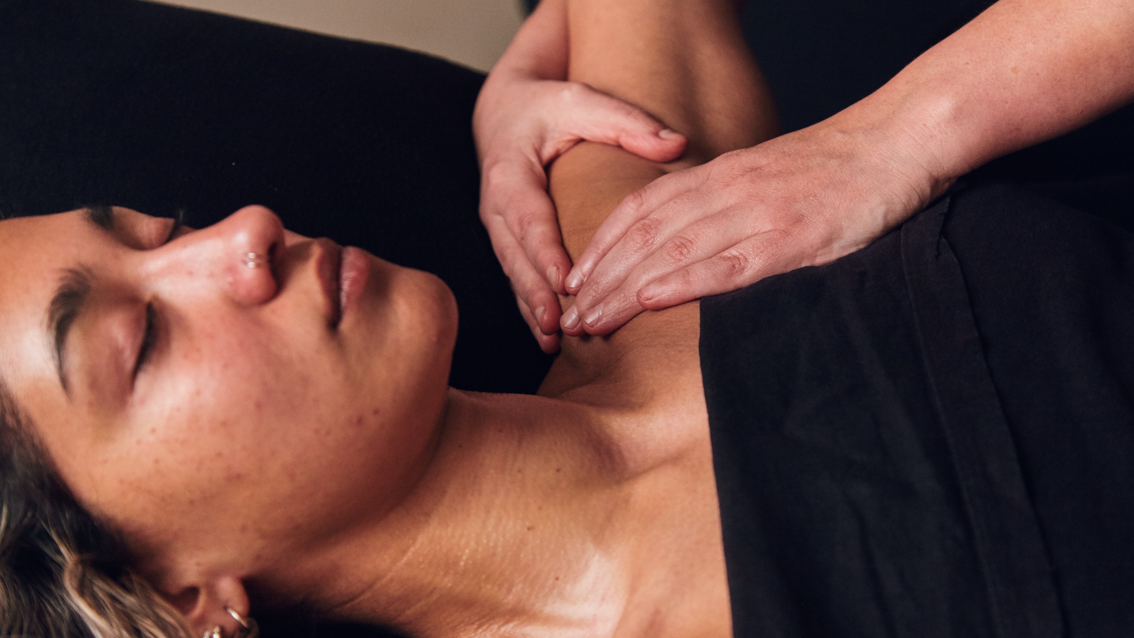 Person lying down, eyes closed having their shoulder massaged. 