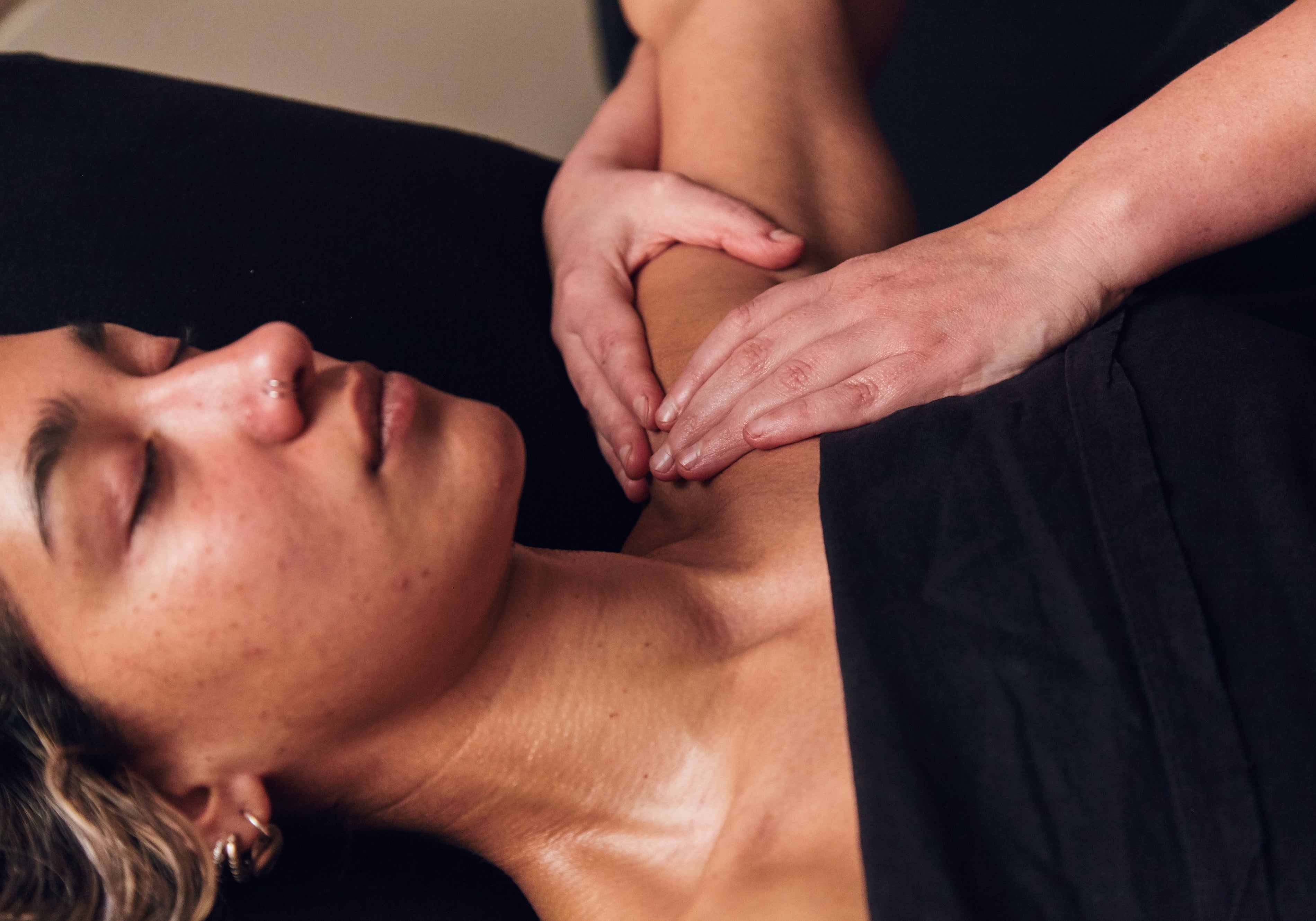 Person lying down, eyes closed having their shoulder massaged. 