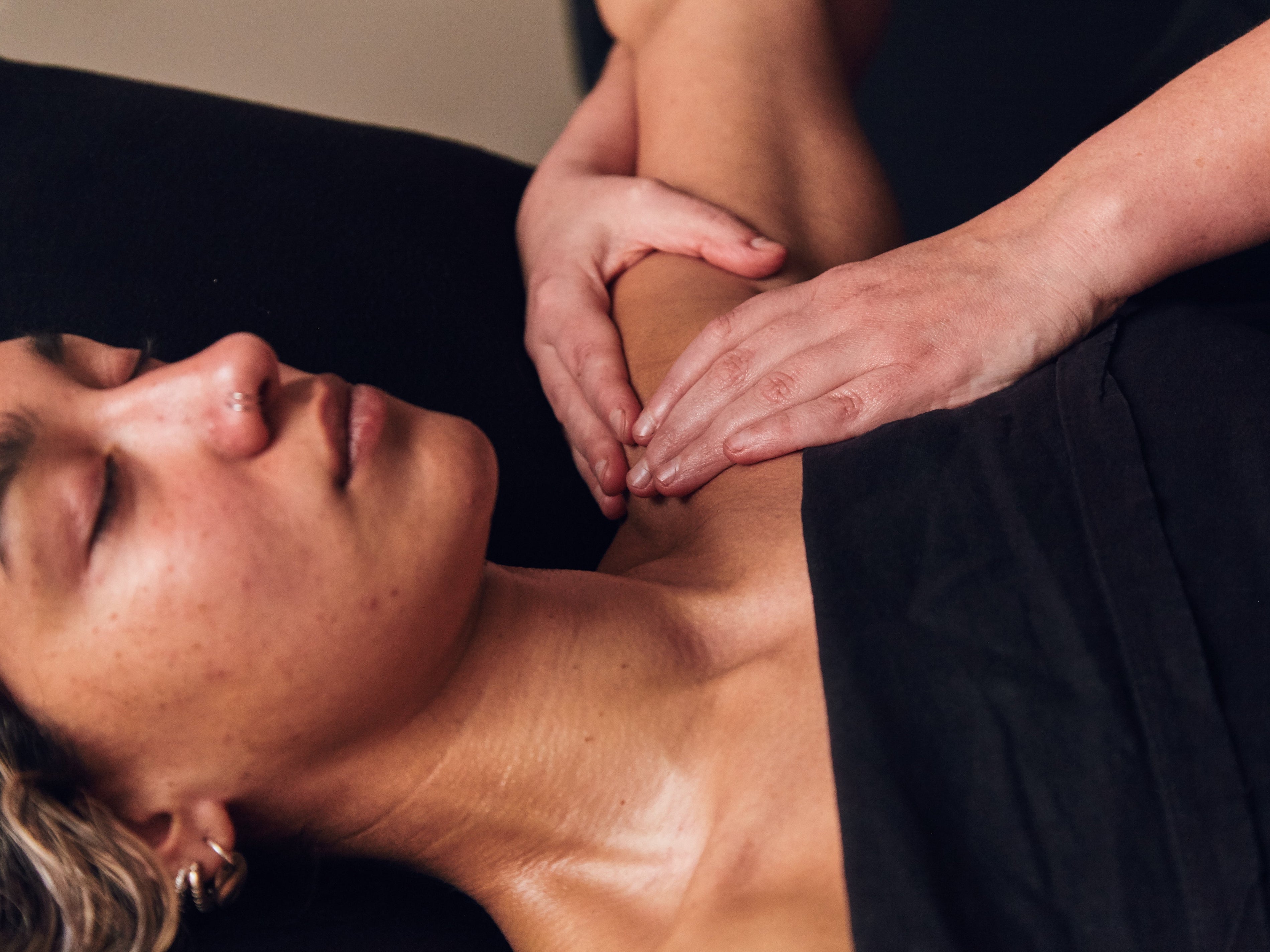Person lying down, eyes closed having their shoulder massaged. 